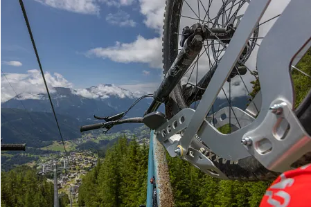 Sessellift mit montierten Bike Cips und eingehängten Mountainbikes fährt in Richtung Bergstation. Blick vom Sessellift an der Befestigung vorbei Richtung Tal.