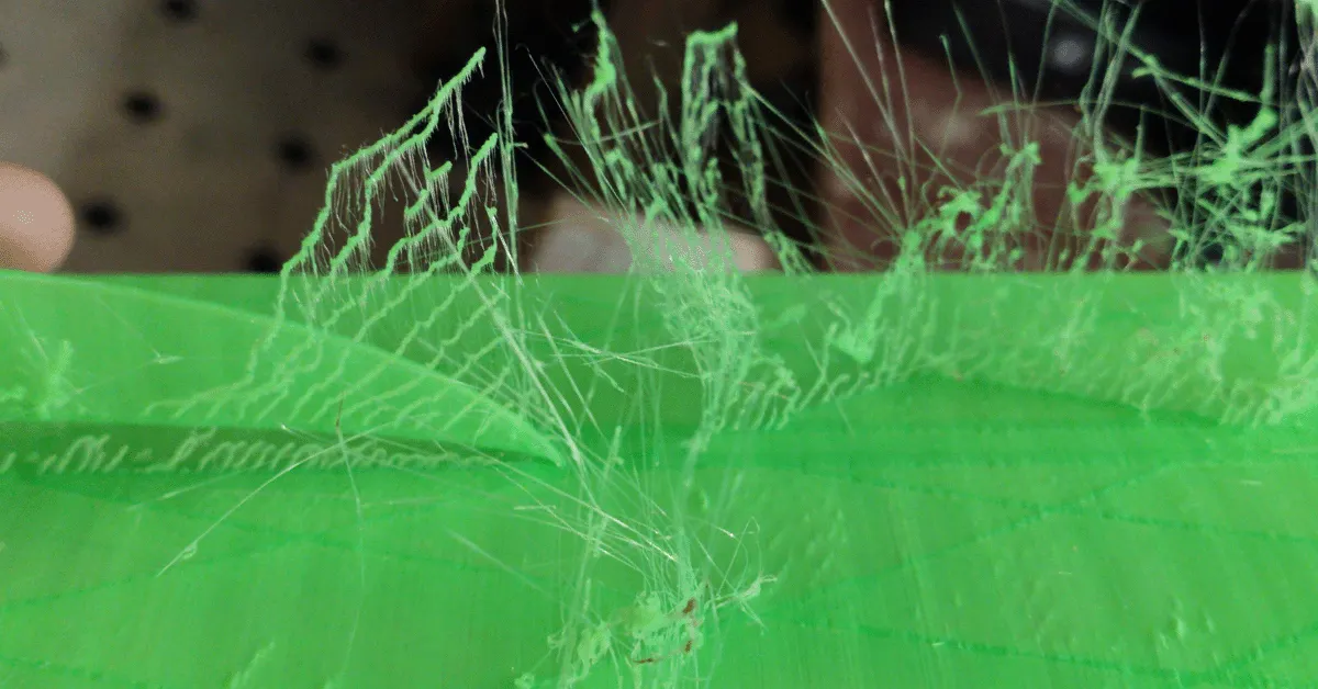 Ein Bauteil, bei dem das neongrüne Filament die fürs "Stringing" typischen Fäden gezogen hat.