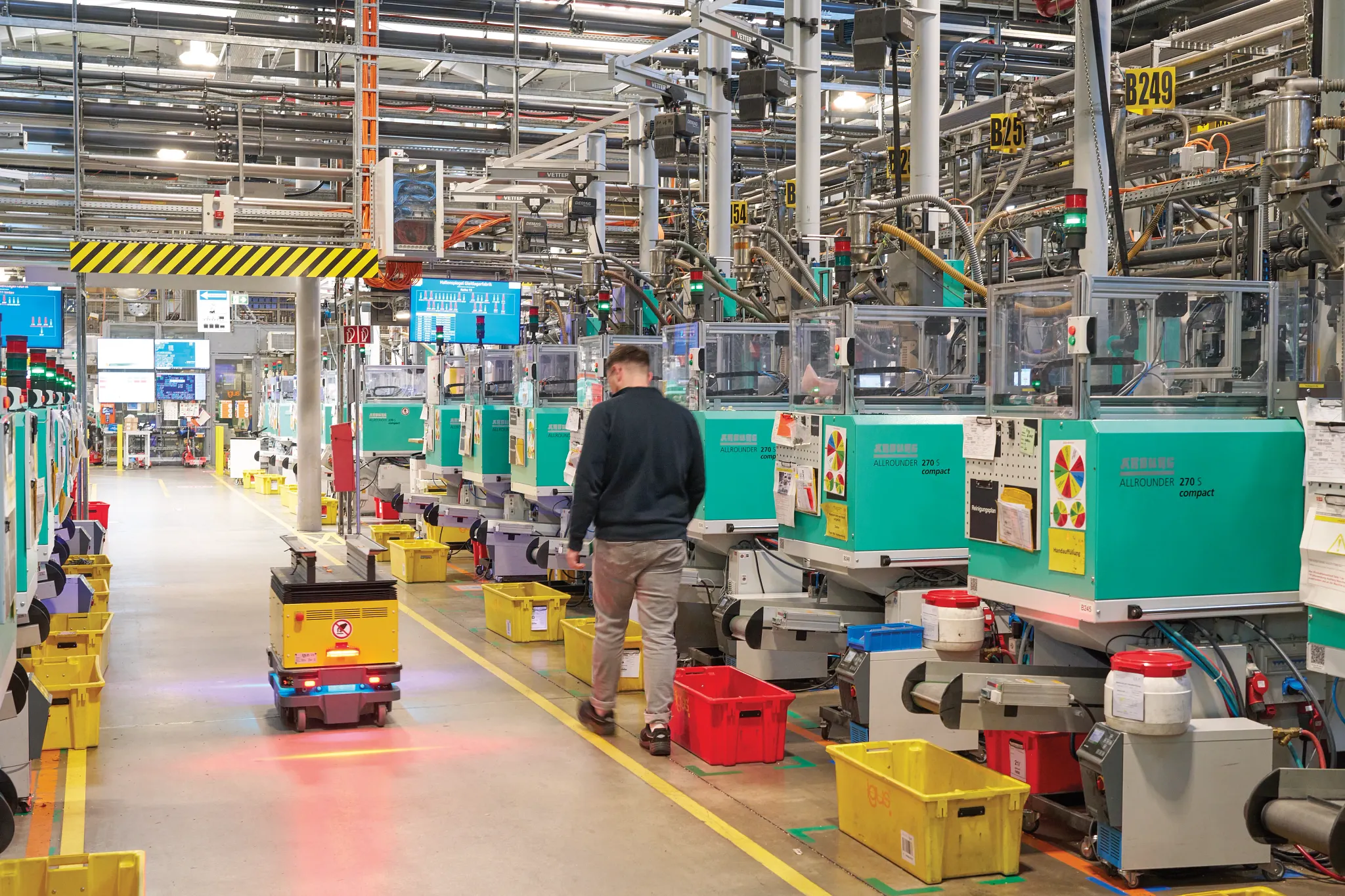 Automated mobile robots transporting bins through an injection molding facility with workers nearby.